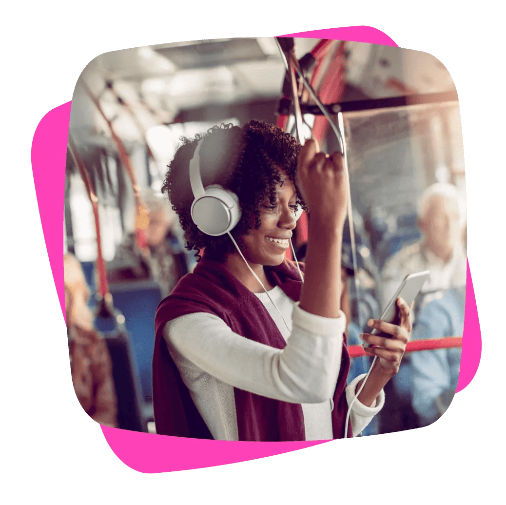 Woman standing inside a public transport bus, with headphones on, and smiling at her phone
